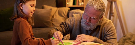 Senior man spending quality time drawing with young girl in comfortable living room setting. Both deeply engaged in creative activity with homey ambianceの写真素材