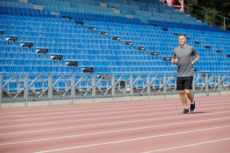 Man jogging on running track in empty stadium during daytime Practicing running on athletic field...