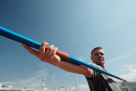 Athlete holding javelin in outdoor sports field with blue sky in background Camera lens capturing intensity and focus during training sessionの写真素材