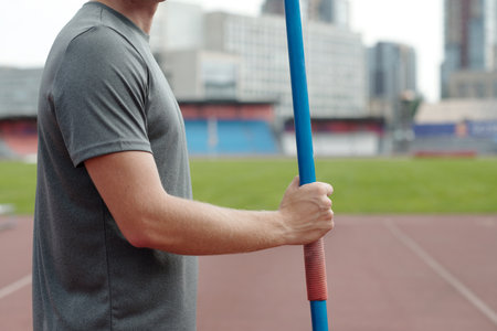 Person holding blue pole on track of an athletic stadium with urban buildings in the background creating contrast between modern cityscape and athletic fieldの写真素材