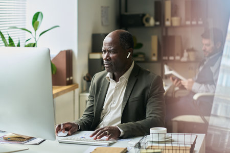 Senior male office worker in formalwear watching online video or looking through information on computer screenの写真素材