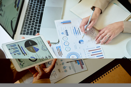 Hands of young businesswoman pointing at paperwork with graphic financial data while her colleague...
