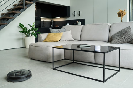 Modern minimalist living room featuring a sectional sofa, glass coffee table, and potted plant near the staircase. Clean lines and neutral colors emphasize contemporary aestheticsの写真素材