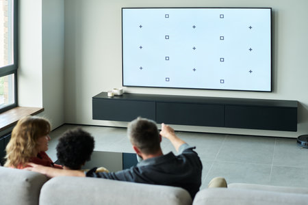 Group of people sitting on a stylish couch, engaged in watching a television with a minimalist design in a modern living room settingの写真素材
