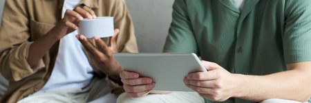 Two people collaborating, one holding tablet while another gestures with coffee cup. Sharing...