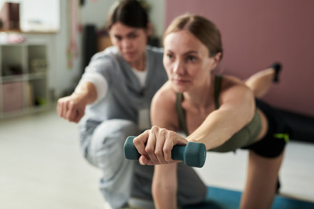 Women engaging in fitness routine while lifting dumbbells in a gym setting with focus and...