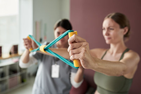 Woman engaging in resistance band exercises with assistance from trainer in fitness studio, focusing on strength training and balance. Both individuals display concentration and determinationの写真素材