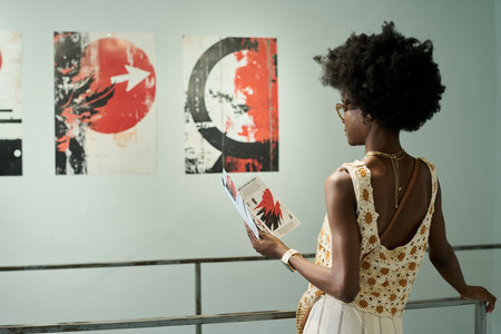 Young elegant African American woman in smart casualwear standing in front of creative artwork in modern galleryの写真素材