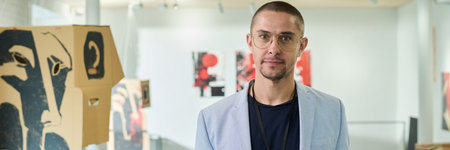 Panoramic of young male manager or owner of modern art gallery looking at camera while meeting new...