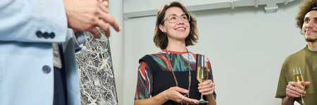 Header of young female visitor of gallery with flute of champagne looking at another person during...