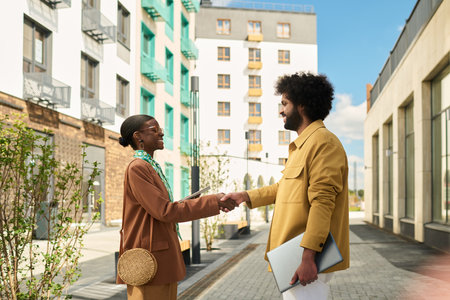 Two professionals exchanging handshake outdoors near modern apartment structures, initiating...