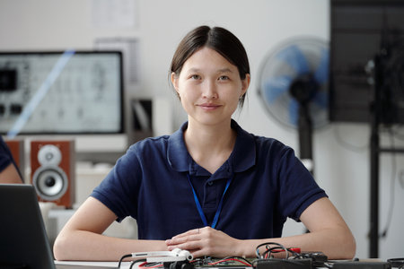 Portrait of Asian woman focusing on electronic circuit project in modern lab setting with laptop and...