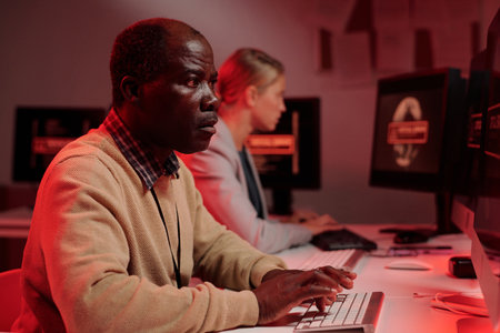 Side view of serious mature security guard trying to solve technical problem while sitting in front...