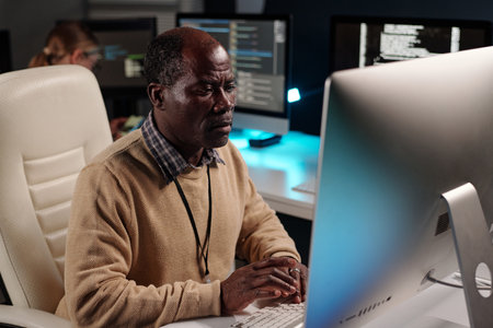 Experienced male IT support manager decoding data while sitting in front of desktop computer monitor...