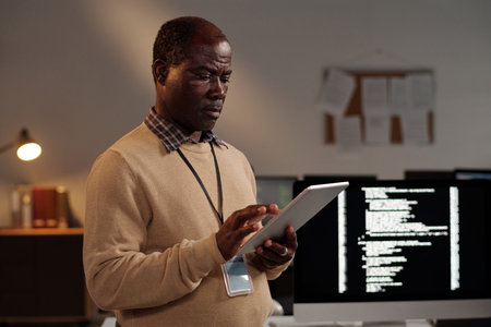 Mature male IT engineer scrolling on tablet screen while decoding online data or testing new...