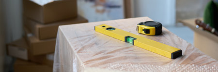 Header of handtool for checking surface level and rolled measuring tape on wooden piece of furniture...