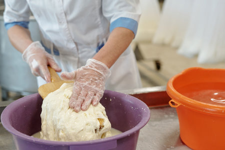 Worker mixing dough manually while wearing gloves in bakery setting, ensuring hygiene and safety during food preparation processの写真素材