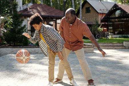 Parent and child enjoying a game of basketball on outdoor court while spending quality time together...