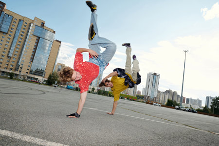 Two breakdancers performing on a concrete surface with skyscrapers in the background, showing...