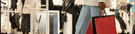 Header of hand and legs of young contemporary female consumer with shopping bags moving along large...