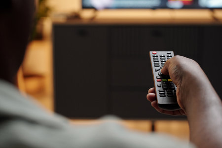 Hand grasping a remote control while aiming at television screen with blurred background creating a symmetrical composition and focusing on activity of relaxingの写真素材