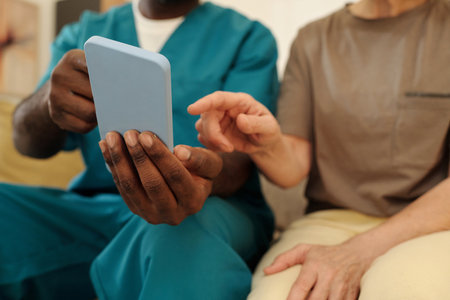 Black nurse and elderly patient examining a tablet together signaling engagement in a healthcare...