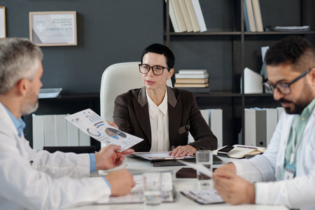 Group of Medical Experts at Meeting Table with Woman Presenting Data Reports in Clinic Officeの写真素材