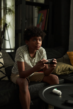 Youthful boy pressing buttons on gamepad and looking at screen of tv set while playing video games...
