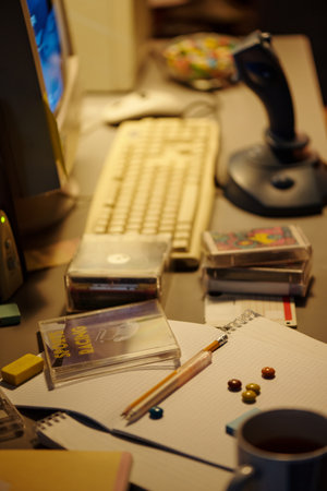 Neatly arranged office desk featuring stationery, gadgets, and computer equipment with stacks of CDs and a pen holder in a dimly lit workspaceの写真素材