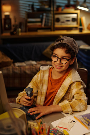 Portrait of young boy smiling while holding flashlight sitting at desk with colorful papers in a...