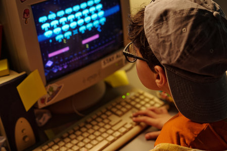 Child enthusiastically engaging with retro video game on older computer setup featuring CRT monitor and vintage keyboard, surrounded by various sticky notes and office suppliesの写真素材