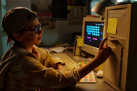 Young boy wearing glasses enthusiastically operating vintage computer in dimly-lit room, surrounded...