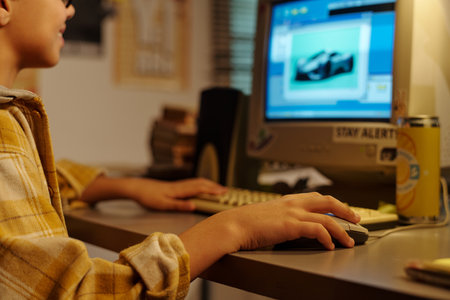Close-up of young boy deeply focused on creating a 3D model on computer screen in a cozy, dimly lit room with various tools and devices around, emphasizing concentrationの写真素材