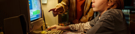 Young child using a computer while receiving direction from an adult in brightly lit room Focused on...