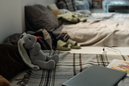 Grey soft toy rabbit sitting in front of laptop and book of comics on warm checkered plaid covering sleeper.の写真素材
