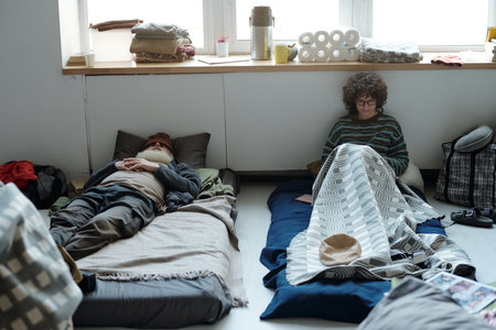 Young female sitting on sleeper and watching video or looking through posts in mobile phone next to napping manの写真素材