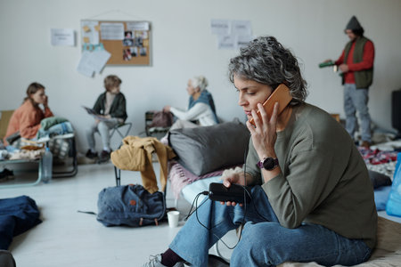 Mature woman in casual attire sitting on sleeper in front of camera and speaking on mobile phoneの写真素材