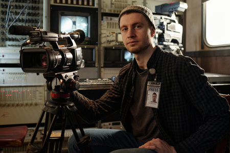 Serious and confident male videographer with professional equipment looking at camera while sitting...