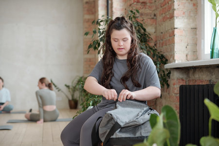 Young woman in activewear zipping bag after training while sitting in gymの写真素材