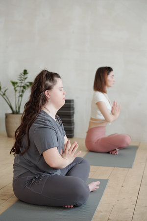 Two girls in activewear sitting in pose of lotus on mats during yoga practiceの写真素材