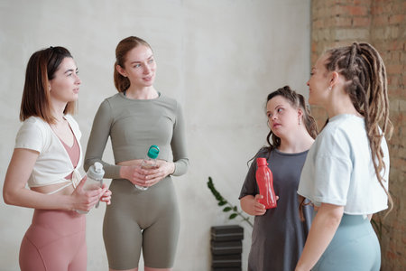 Restful girls discussing new yoga exercises and having water at breakの写真素材