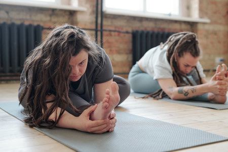 Female doing difficult stretching exercise on mat during yoga training in gymの写真素材
