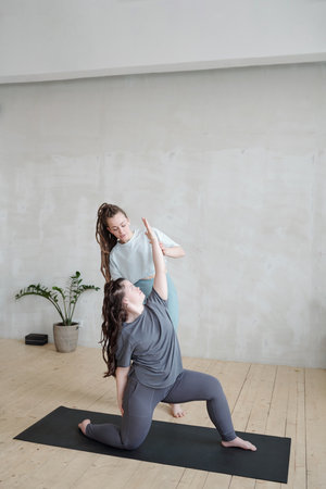 Young yoga trainer consulting and helping female with stretching and balance exercise during workoutの写真素材