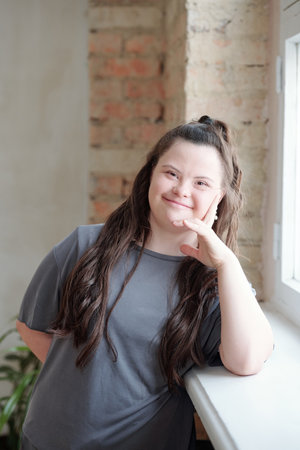 Happy girl in grey sportswear looking at you while leaning by windowsillの写真素材