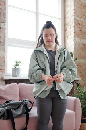 Brunette female in sportswear standing in front of couch in living-roomの写真素材