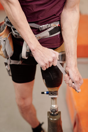Young man with physical disability fixing climbing equipment before training