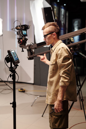 Young cameraman looking at display on tripod during video shooting
