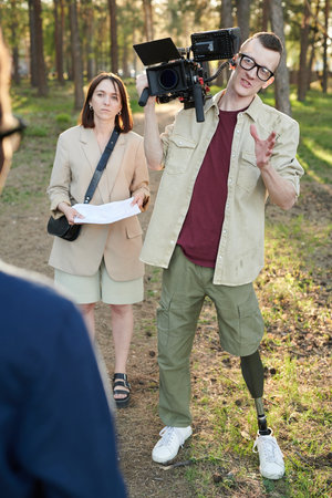Disabled operator with camera talking to man during outdoor video shooting