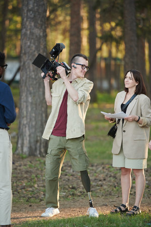 Happy disabled operator and his female assistant talking during outdoor video shooting