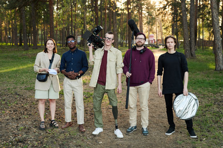 Large intercultural video shooting group with equipment standing in the forest